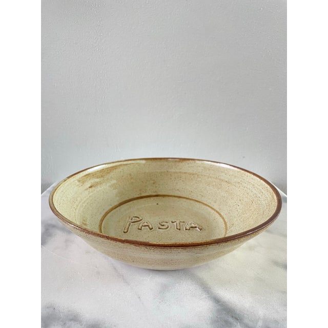 A vintage studio ceramic bowl with tan and brown glaze and “pasta” decoration at the bottom of the bowl.