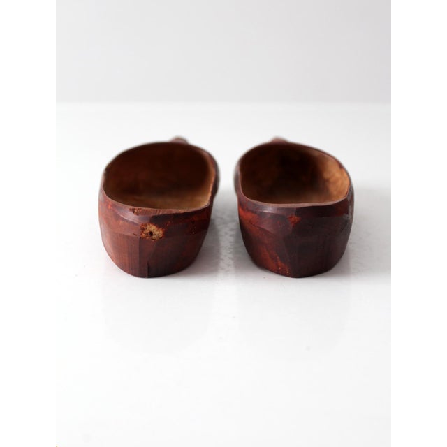 Vintage pair of carved wood clogs with a rich reddish-brown finish and incised geometric designs across the toes. Their...