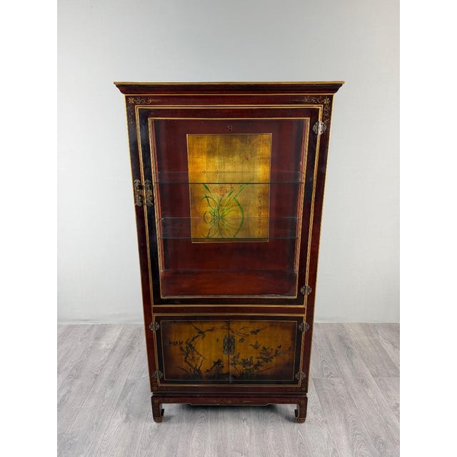 An elegant display cabinet in stained wood, richly decorated with gilt trim and delicate floral motifs. the upper section...