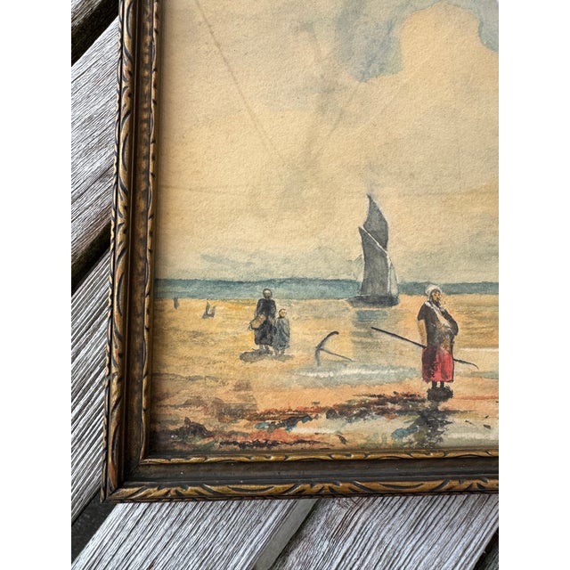 Framed watercolor depicting a quiet coastal scene with a beached fishing boat and figures along the shoreline. Soft, muted...