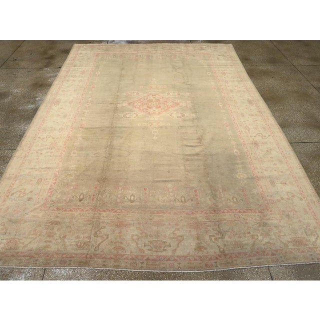 An antique Turkish Oushak room size carpet. A light open field is centered by a flattened diamond medallion and is framed...