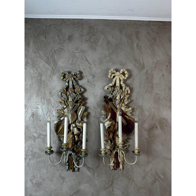 A charming pair of louis xvi style wooden wall sconces, richly decorated with musical motifs. each sconce features a...