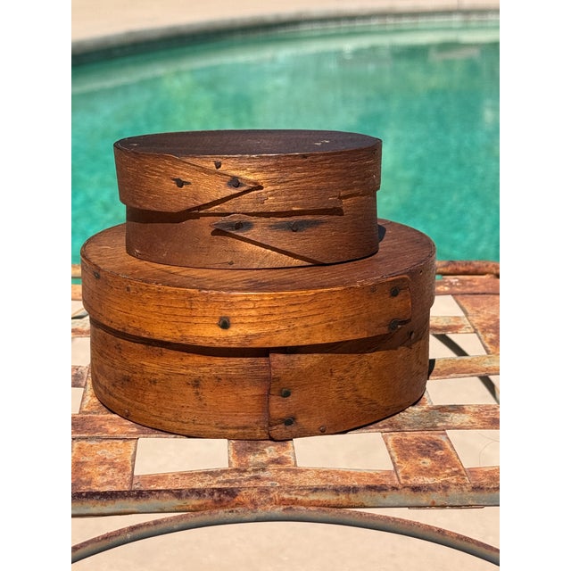 A pair of antique bentwood boxes in the Shaker tradition, comprising one oval and one round example, both displaying the...