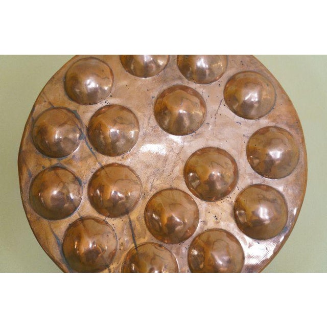 A substantial vintage copper multi-cup mold pan featuring a large round form, raised rounded wells, and decorative brass...