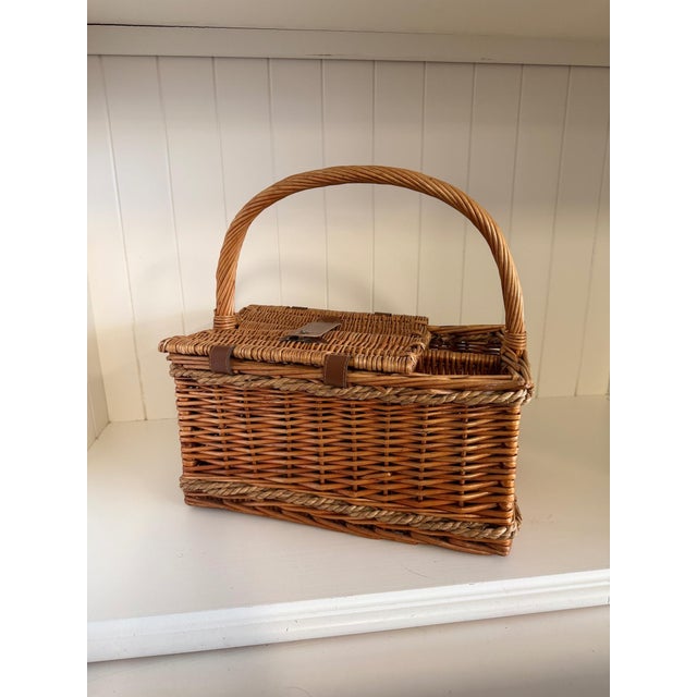 A beautifully woven vintage wicker picnic basket featuring a generous arched carrying handle, hinged lid with leather...