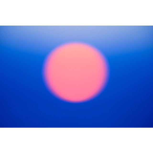 This photographic work presents a softly blurred orb in shades of pink against a gradient of deep blue, evoking a serene...