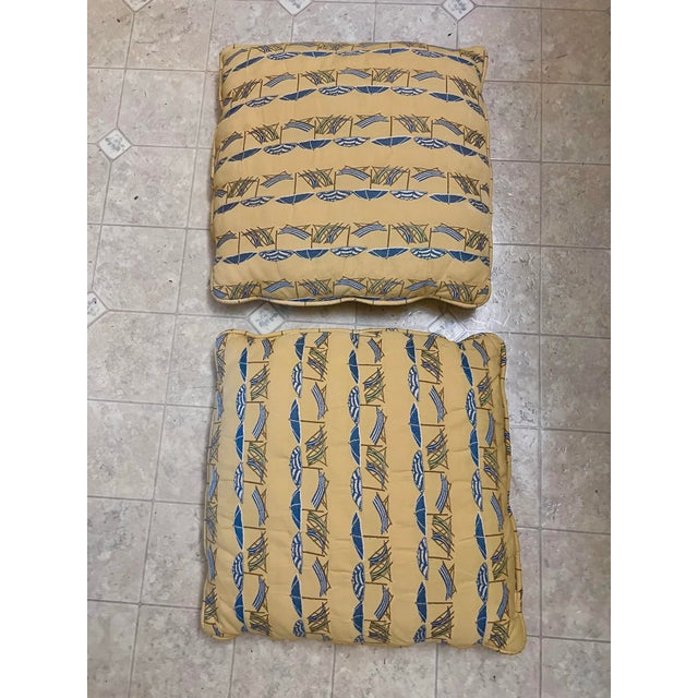 These yellow throw pillows feature a repeating nautical umbrella and lounge chair patterns in blue. Piping trim around...