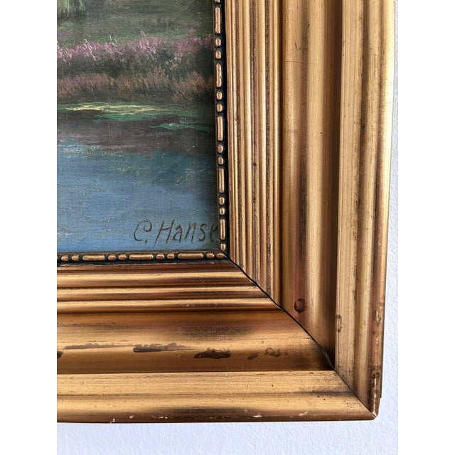 This original vintage oil painting from the 1930s shows a peaceful river landscape with trees, water, and soft blue sky....