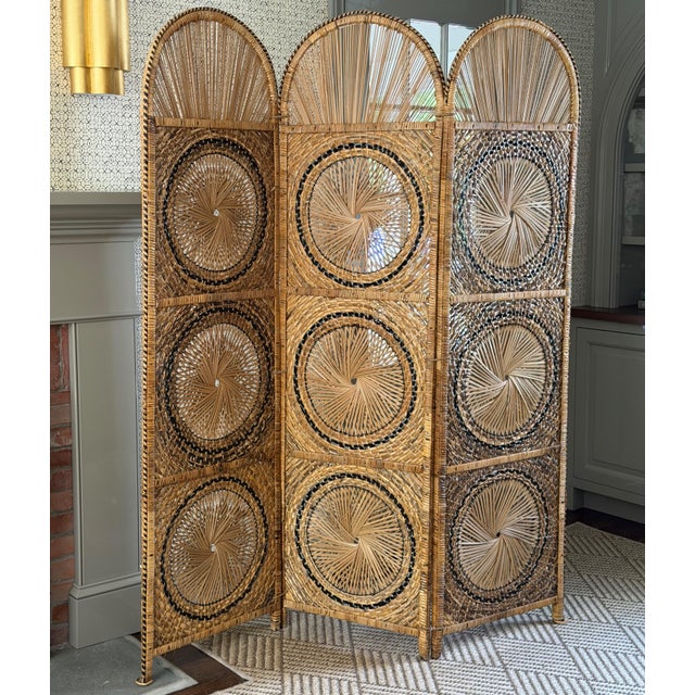 A vintage woven rattan folding screen featuring, arched panels and intricate handwoven sunburst motifs throughout. This...