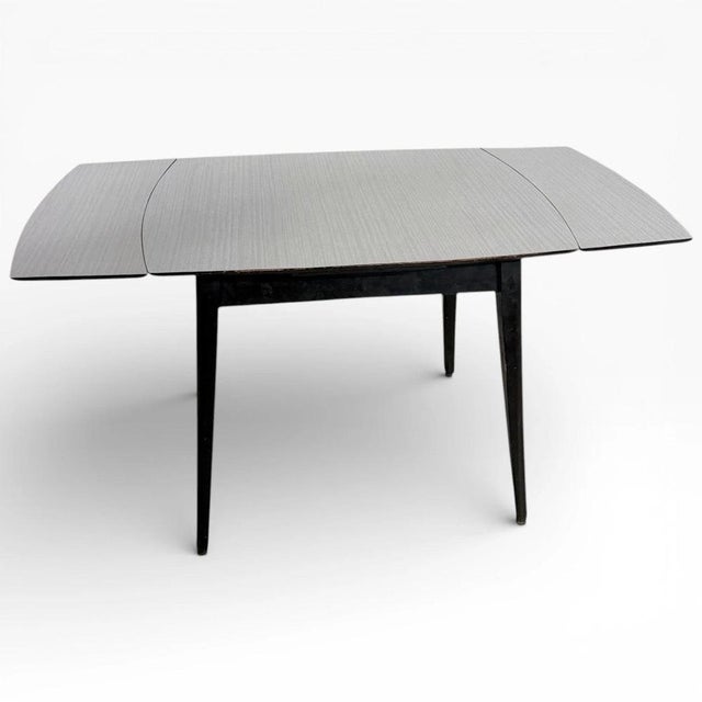 The extendable dining table offers a practical dining solution with a crisp white Formica table top and sleek black leg...