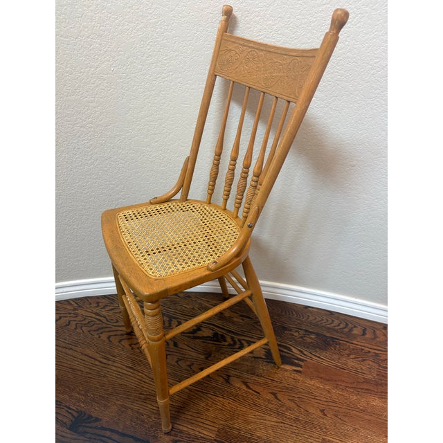 Charming antique American oak youth dining chair dating to circa 1900, featuring an ornate floral pressed-back crest,...