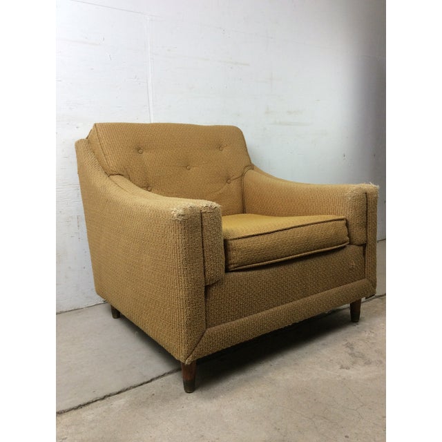 This mid century modern lounge chair features original yellow upholstery and small tapered legs with brass capped feet.