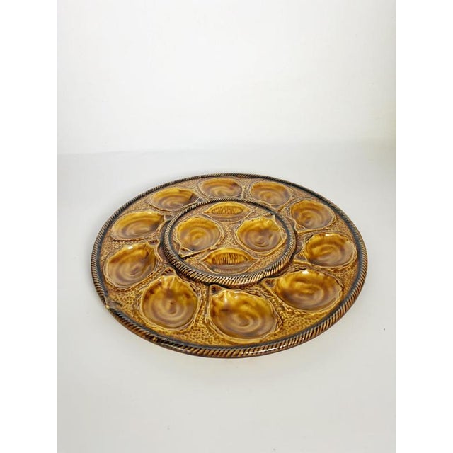An elegant glazed ceramic serving platter designed for oysters. It features twelve individual wells arranged in a circle,...