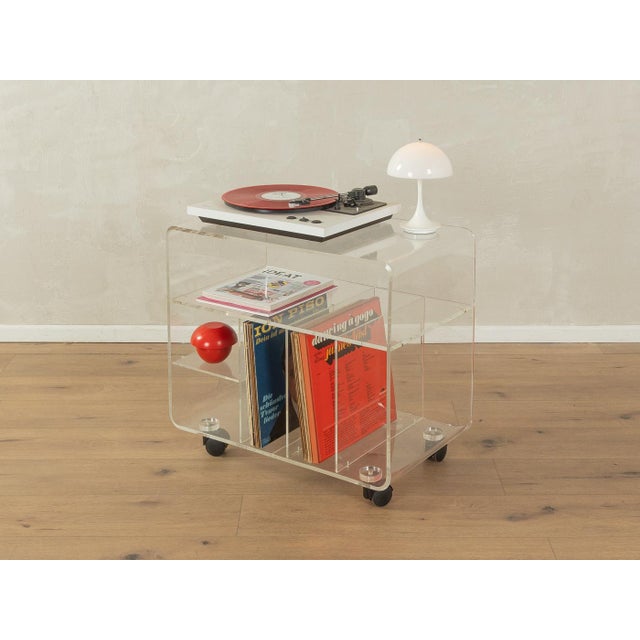 Rare hi-fi rack from the 1960s. Acrylic glass frame with two shelves, three record compartments, and plastic wheels....