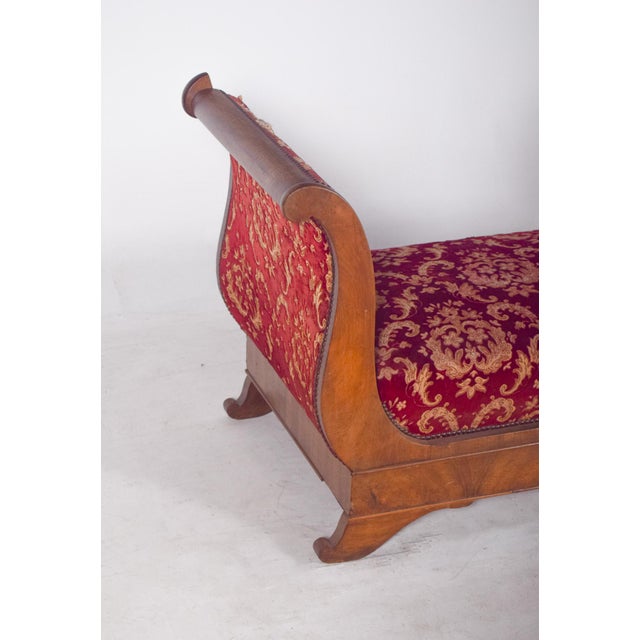 Empire-style canapé, upholstered in red fabric. Characterized by its sturdy structure in light-toned wood with a varnished...