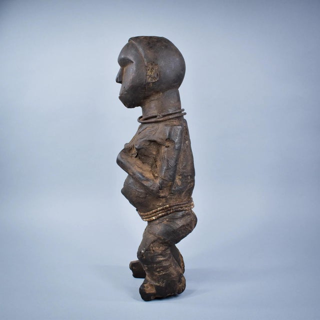 This hand-carved wooden figure represents a stylized human form with a pronounced head, simplified facial features, and a...