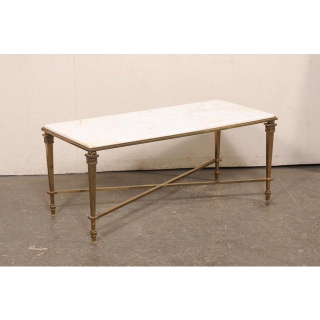 A French brass coffee table, with marble top, from the mid 20th century. This mid-century coffee table from France...