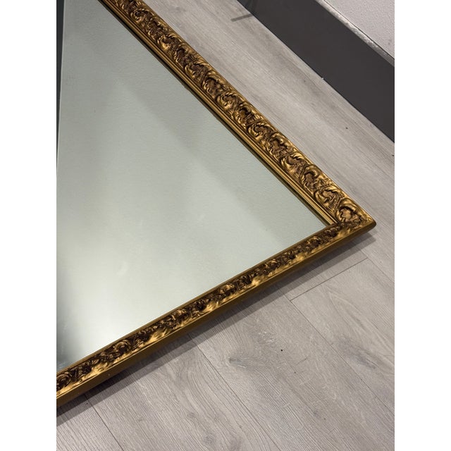 Striking vintage rectangular wall mirror featuring an ornate gilt frame with richly carved scrolling and floral detailing....