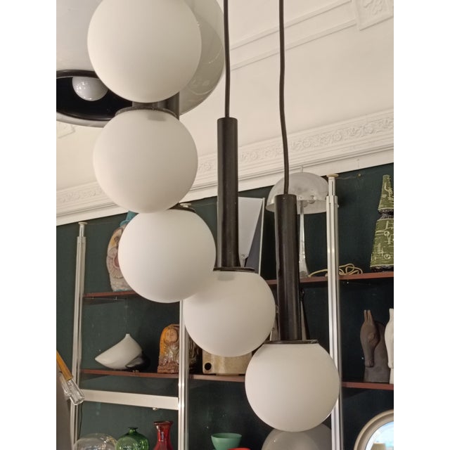 Cascade-style pendant lamp featuring 12 white opal glass spheres and a black metal frame. Made in Italy. The design...