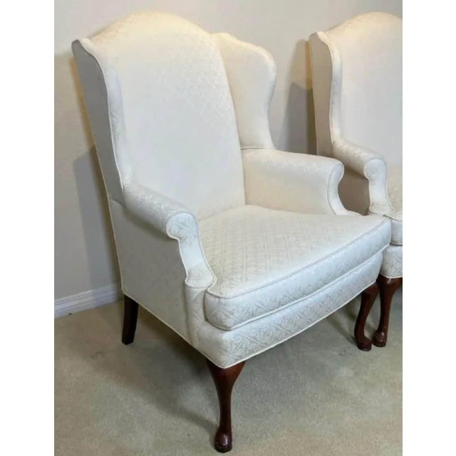 Elegant pair of traditional wingback lounge chairs featuring classic Queen Anne styling with carved cabriole legs in a...