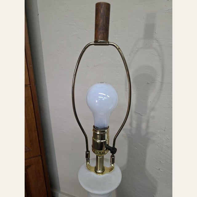 This is a tall 1970s Mid-Century Modern white ribbed ceramic table lamp with a dark wood base, brass-tone hardware, and a...