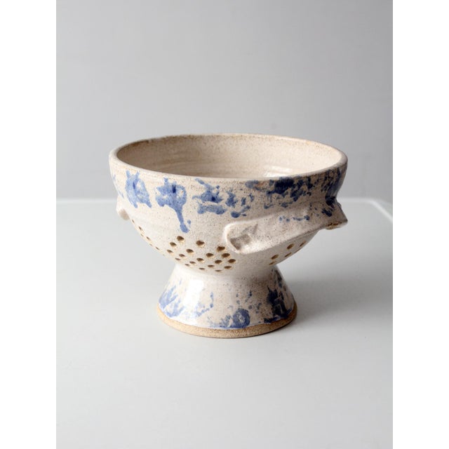 A vintage handmade studio pottery colander dated 1986, featuring a speckled cream glaze accented with loose cobalt blue...