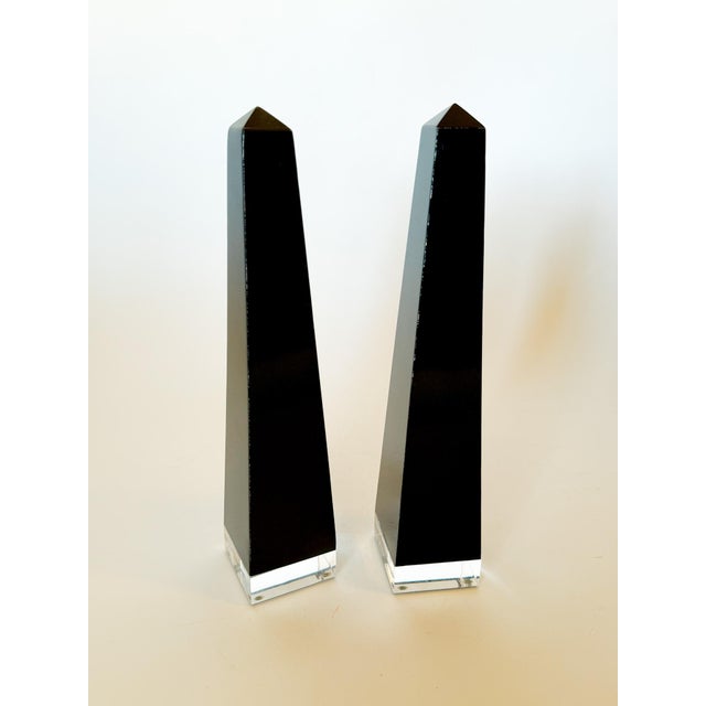 A striking pair of modern black lucite obelisks set on clear lucite platforms. This stunning set has a glossy finish and a...