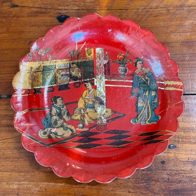 A single red lacquered papier mache wine coaster with a scalloped rim, decorated with a Japanese tea scene — figures in...