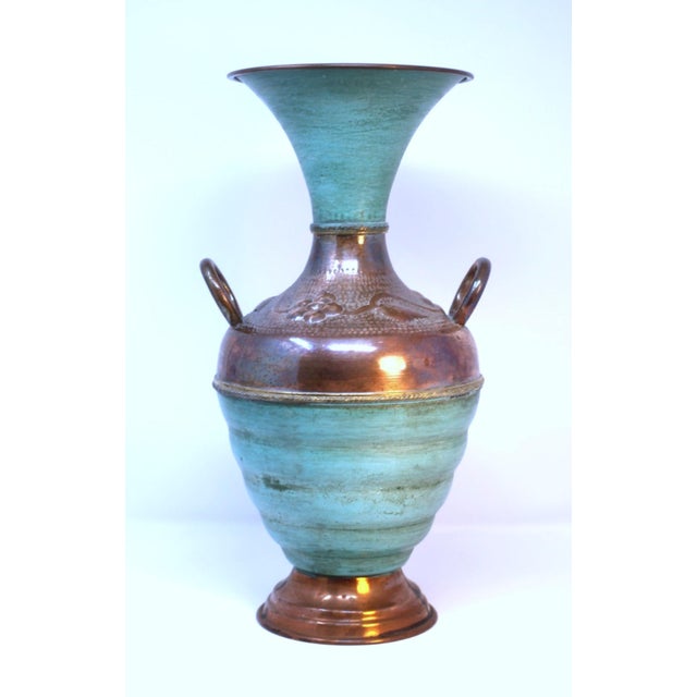 This vintage vase combines hammered copper and a smooth green patina in a floral motif with a flared neck and copper handles.