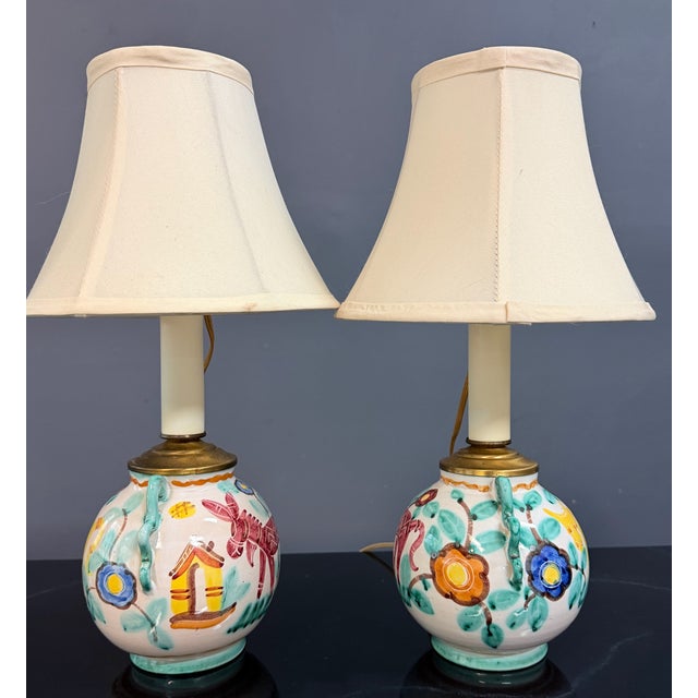 Charming pair of Italian ceramic bedside lamps featuring whimsical hand-painted animal motifs in rich jewel tones against...