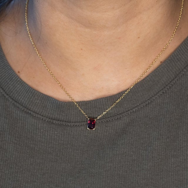 A natural red spinel glows with vivid, fiery red in this solid 14K yellow gold solitaire pendant, hung on an included fine...