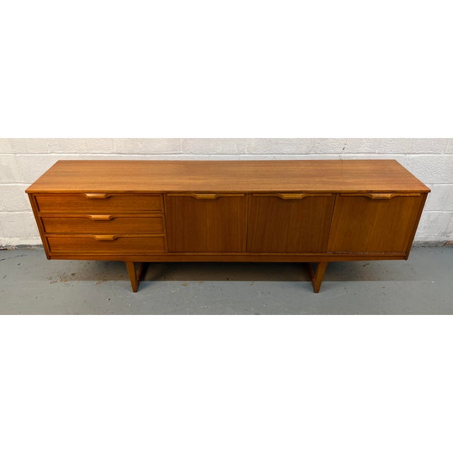 This vintage Mid-Century Modern sideboard was manufactured by Stonehill Furniture in England and features distinctive sled...