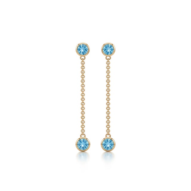 The earrings are adorned with vibrant, round-cut natural blue topaz gemstones that offer a bright, captivating sky-blue...