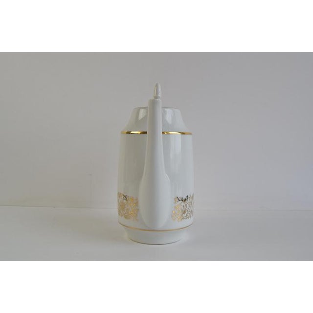 This mid-century piece features a sleek white body adorned with refined gold floral motifs and a gold accent band around...