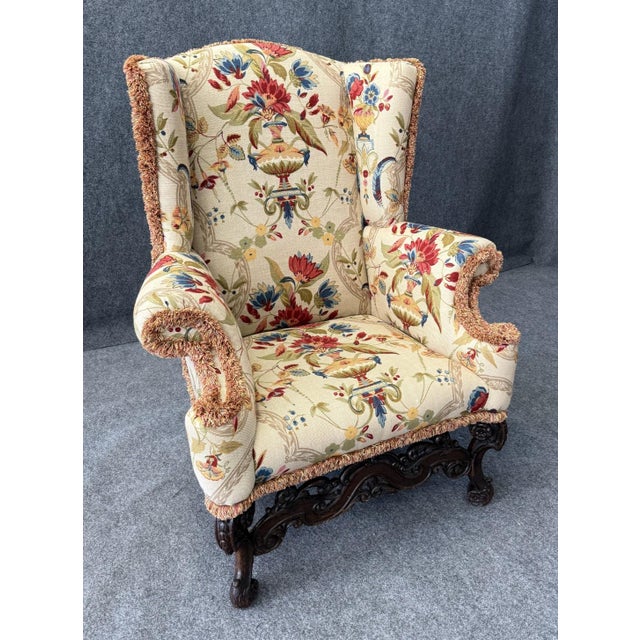 This early 1800s wingback armchair features an intricately carved wooden base with scrolled details, showcasing the...