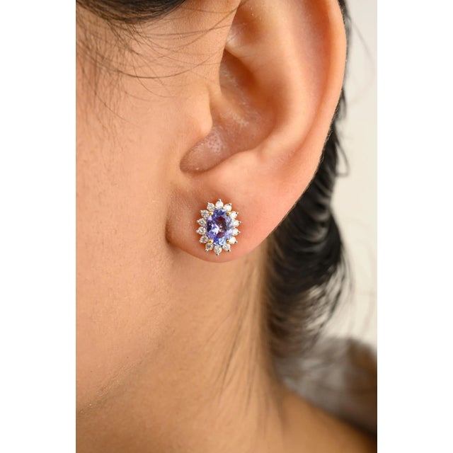 These exquisite stud earrings showcase natural oval-cut tanzanite, each surrounded by a stunning halo of diamonds. The...