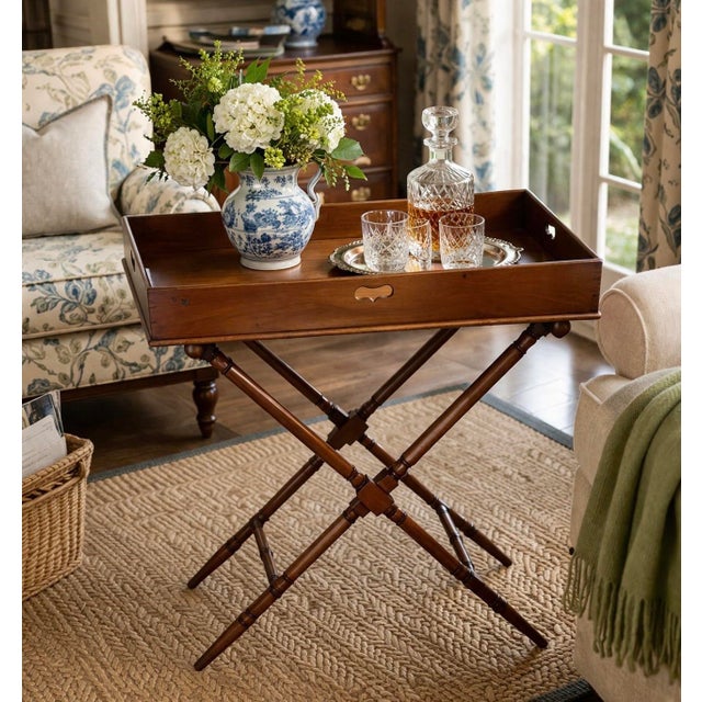 A classic vintage mahogany butler’s tray table featuring a removable rectangular tray with elegant cutout handles and a...