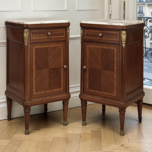 A fine pair of French Louis XVI style antique nightstands in mahogany, combining geometric marquetry, original marble tops...