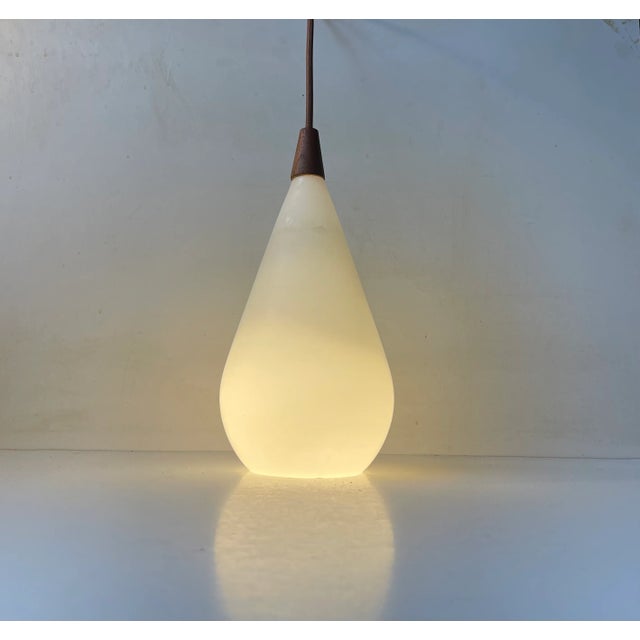 A simple Swedish Modern pendant light constructed of a blown matte opaline glass and a stylish top in solid teak. Designed...