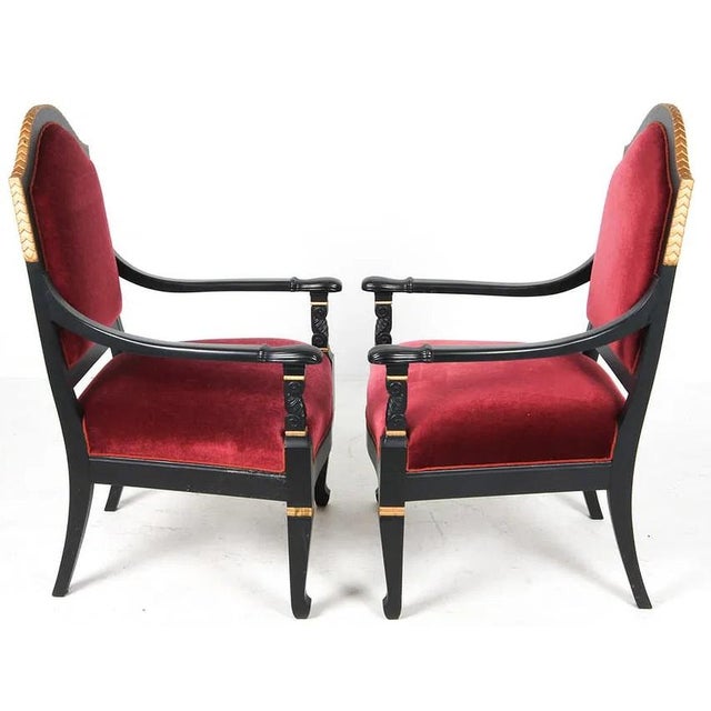 A pair of French Empire revival armchairs upholstered in a deep burgundy mohair fabric. The chairs have an ebonized finish...