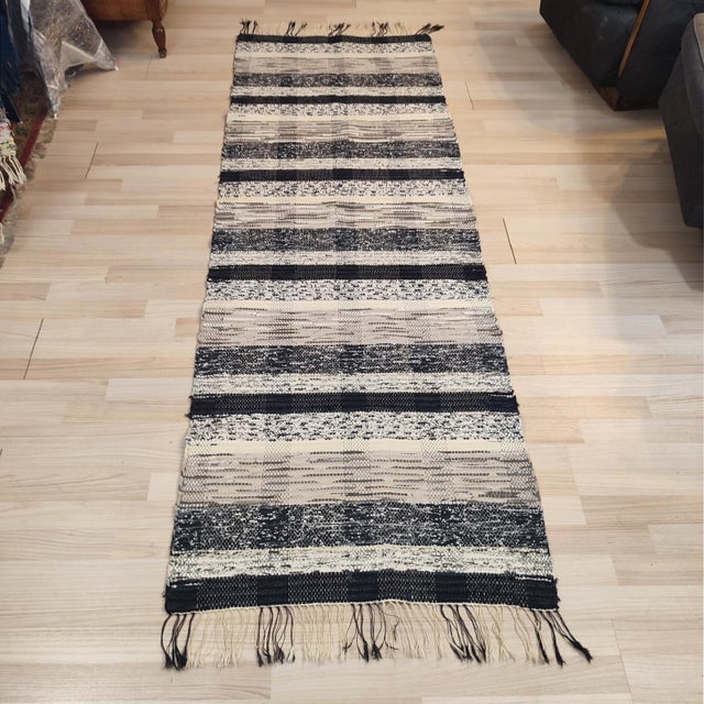 A mid-20th-century Swedish rag rug, it features a geometric stripe design in muted ecru, white, grey, and black tones....