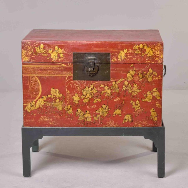 Red lacquered trunk adorned with gilt figural scenes depicting children at play and daily life activities. The decoration...