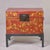 Red lacquered trunk adorned with gilt figural scenes depicting children at play and daily life activities. The decoration...