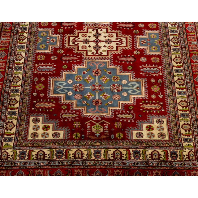 Indian Kazak Style Wool Carpet, with geometric design on a red ground, label to underside. 9' 7" L x 6' W. Provenance:...