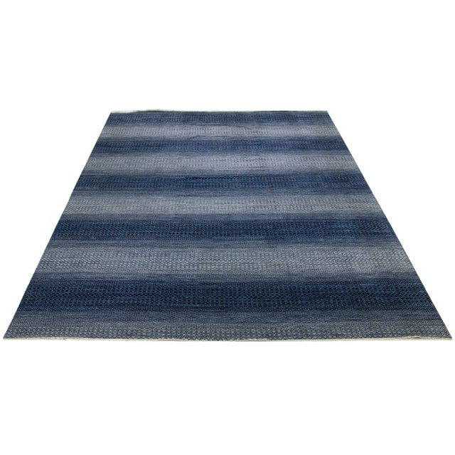 This hand-knotted oversized wool rug showcases a modern design characterized by a blend of gray and navy blue tones,...