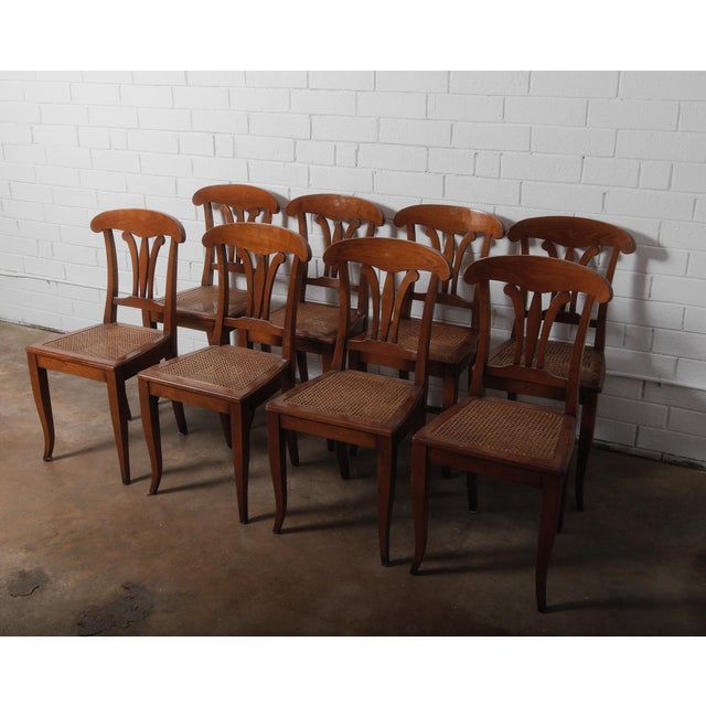 This elegant set of eight dining chairs showcases refined Neoclassical influence with graceful lines and warm cherry-toned...