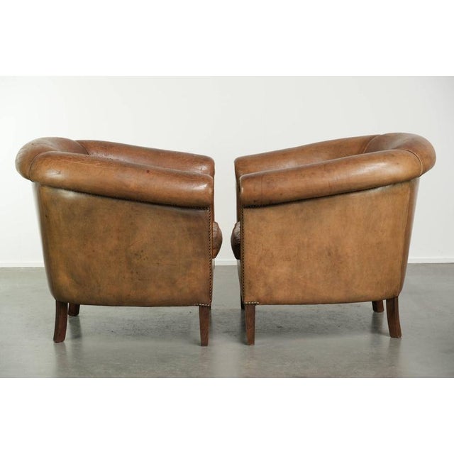 This sturdy set of 2 large vintage sheepskin club armchairs features a beautiful patina. The armchairs have loose seat...