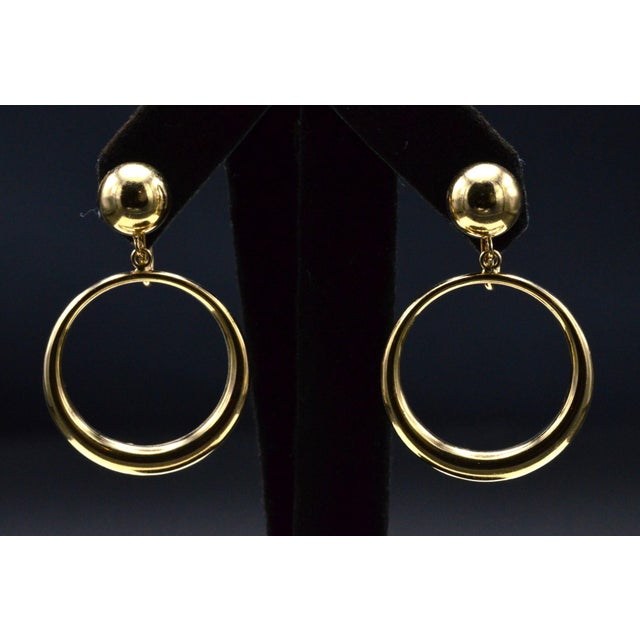 The McHenry: Yellow Gold Statement Earrings. The earrings feature a top polished ball with a dangling crescent circle to...