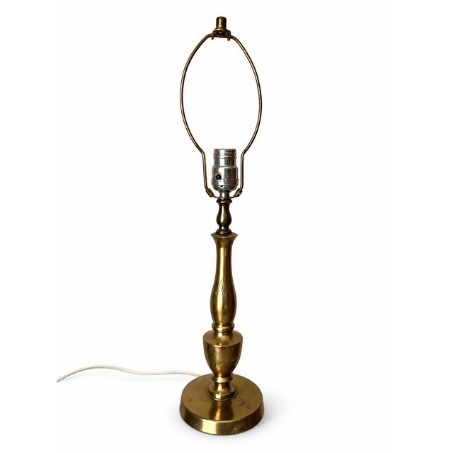 A tall, slender baluster table lamp with a warm brass-tone finish and delicate etched decoration on its stem and urn-...