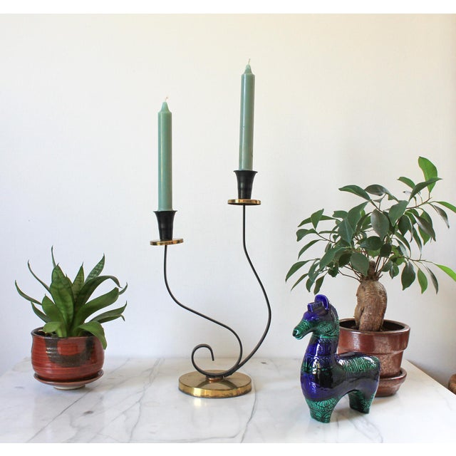 Mid-century black metal and brass scrolled double-candle holder features asymmetric curved stems and a circular brass-...